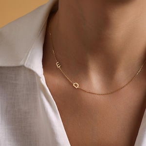 May include: A gold chain necklace with two small letters, "E" and "D", hanging from it. The necklace is worn by a person with a white shirt.