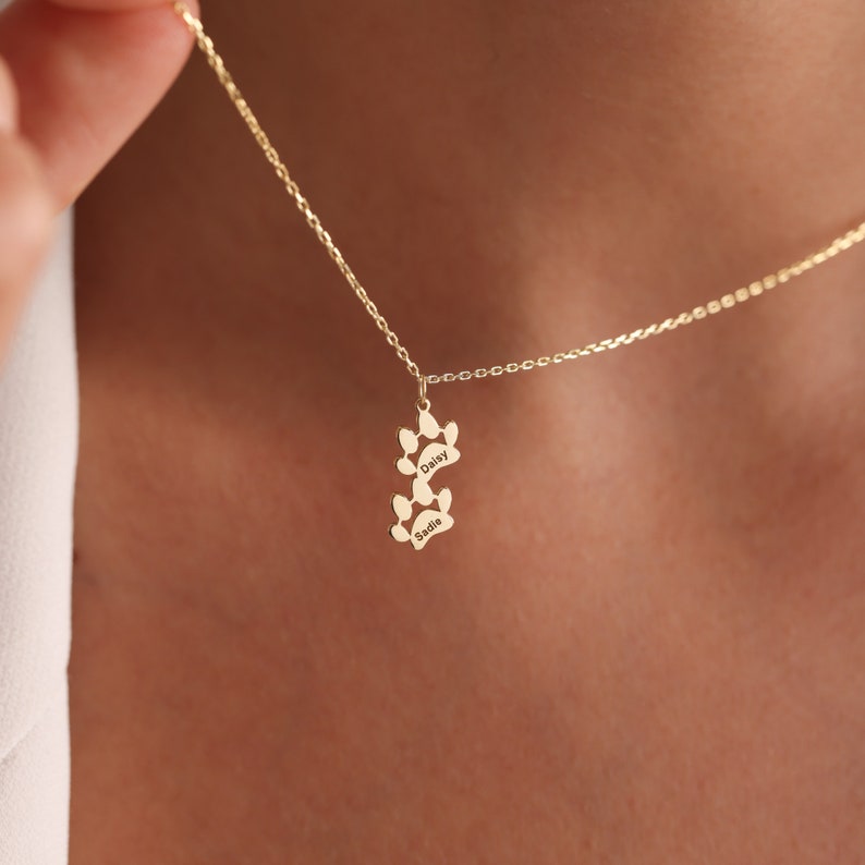 May include: Gold necklace with a double paw print charm. The charm is engraved with the names "Daisy" and "Sadie".