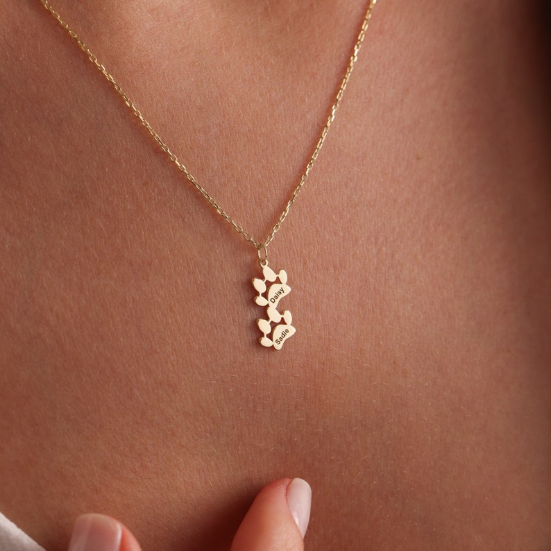 May include: Gold necklace with a paw print charm engraved with the names Daisy and Sadie.