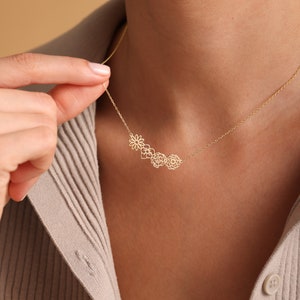 K&ouml;nnte beinhalten: Eine goldene Halskette mit einer zarten Kette und einem Anh&auml;nger mit einer Gruppe von vier ausgeschnittenen Blumenmotiven.