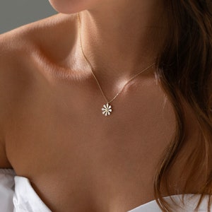 May include: A delicate gold chain necklace with a small white flower pendant.