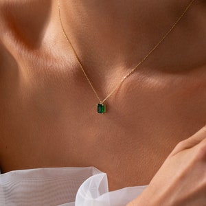 May include: A delicate gold chain necklace with a small emerald green gemstone pendant.