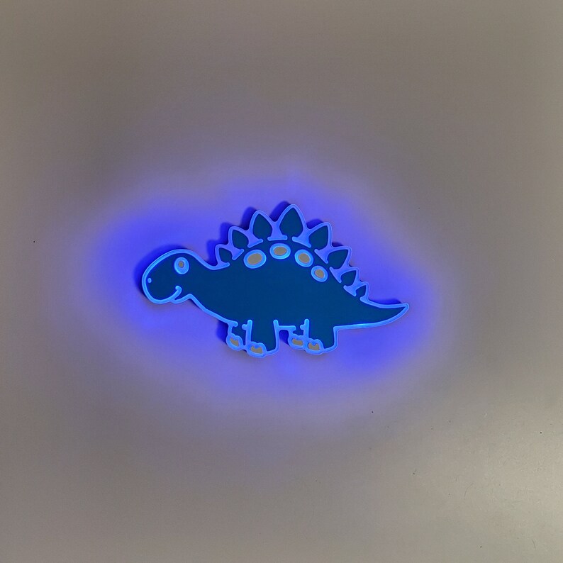 May include: A blue dinosaur-shaped night light with a white outline glows with a blue light.