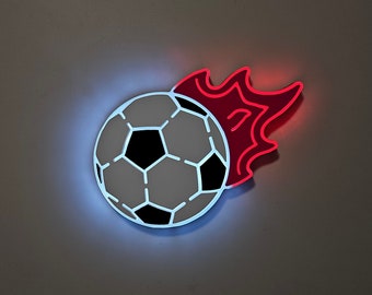 Puede incluir: Un balón de fútbol blanco con paneles negros está en llamas. Las llamas son rojas y naranjas y están detrás del balón. El balón está iluminado desde el frente.