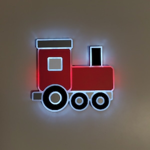 May include: A red and white plastic toy train night light with a white outline. The train has three wheels and a chimney.