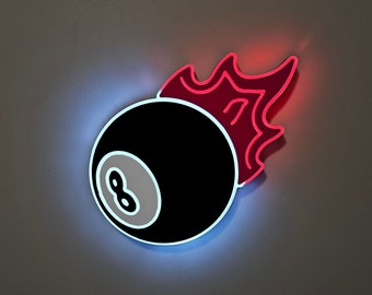 May include: A neon sign featuring a black eight ball with a white number eight and a red flame design. The sign has a blue and red glow around the edges, creating a striking visual effect. The sign is mounted on a gray wall.