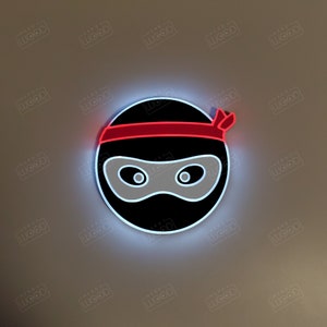 May include: A black and white ninja silhouette with a red headband. The ninja is wearing a mask and has a serious expression.