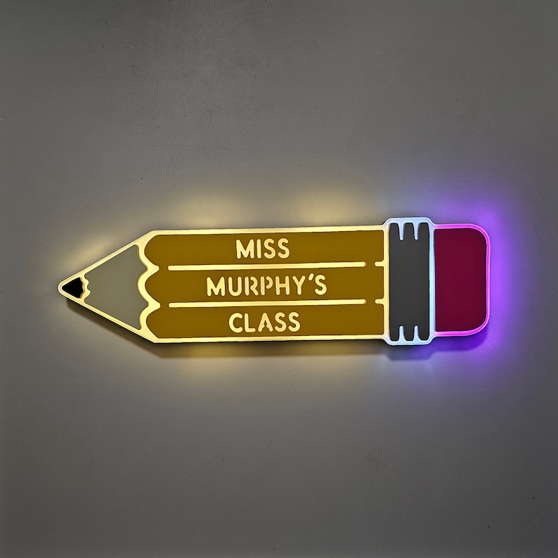 K&ouml;nnte beinhalten: Ein gelbes, bleistiftf&ouml;rmiges Schild mit dem Text "Miss Murphy's Class" in Wei&szlig;. Der Radiergummi ist rosa und der Bleistift ist lila umrandet.