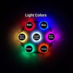 May include: A white circular device with seven different coloured lights. The lights are labelled: Red, Blue, Warm White, Bright White, Pink/Purple, Green, and Orange. The device is labelled "Light Colors".