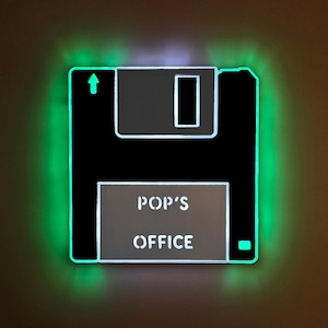May include: A black and white LED light shaped like a floppy disk, with the words "POP'S OFFICE" in white. The light has a green neon glow around the edges and an arrow symbol.