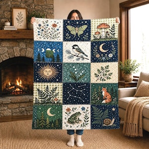May include: A rectangular quilt featuring a grid of fifteen panels with nature-themed illustrations including a moth, mushrooms, a bird, a crescent moon, a sun, lily of the valley, a fox, a frog, a snail, ferns, pine trees, and constellations.