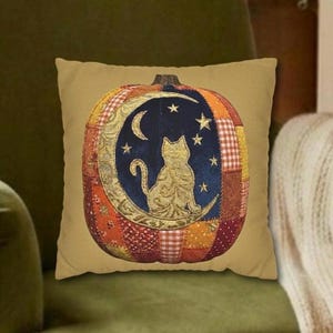 May include: A square throw pillow in a tan color featuring a central pumpkin-shaped graphic. The pumpkin is composed of various patchwork patterns in orange, red, and brown, with a dark blue center depicting a cat sitting on a crescent moon.