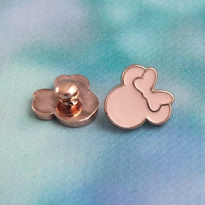 May include: Two metal buttons, one with a white outline of a hand shape and the other with a metal back and a white outline of a hand shape.