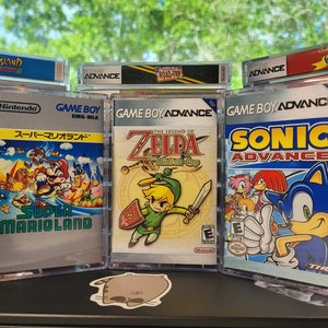 May include: Three Game Boy Advance video game cartridges in clear plastic cases. The cartridges are for the games Super Mario Land, The Legend of Zelda: The Minish Cap, and Sonic Advance. The cartridges are displayed on a shelf with other video game cartridges.