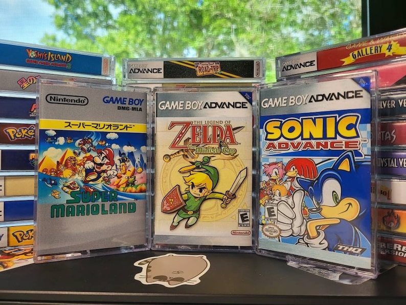 May include: Three Game Boy Advance video game cartridges in clear plastic cases. The cartridges are for the games Super Mario Land, The Legend of Zelda: The Minish Cap, and Sonic Advance. The cartridges are displayed on a shelf with other video game cartridges.