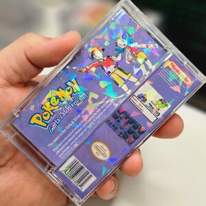 May include: A clear plastic case with a holographic image of two cartoon characters from the Pokemon video game series. The case is for a Game Boy Color game cartridge. The text on the case reads "Pokemon Gotta catch 'em all!" and "The latest in the Gold & Silver series".