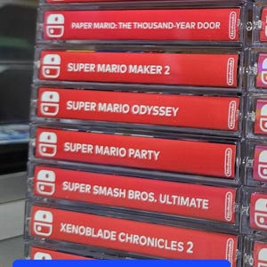 May include: A stack of red Nintendo Switch game cartridges with white text and logos. The games include Mario Golf: Super Rush, Metroid Dread, Paper Mario: The Thousand-Year Door, Super Mario Maker 2, Super Mario Odyssey, Super Mario Party, Super Smash Bros. Ultimate, and Xenoblade Chronicles 2. The text "Standard Spines" and "Applies to Switch ONLY" is at the bottom of the image.