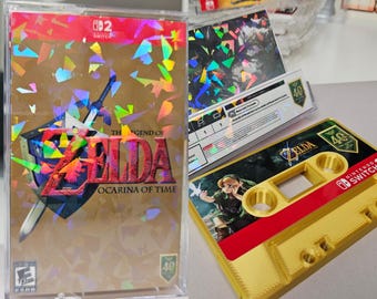 May include: A Nintendo Switch game case for The Legend of Zelda: Ocarina of Time with a gold holographic cover, alongside a gold-colored cassette tape featuring an illustration of Link and the Nintendo Switch logo on a dark green background.