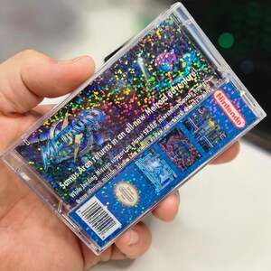 May include: A clear plastic case with a holographic image of the video game Metroid Fusion. The case has a blue background with a silver and black logo. The text on the case reads "Samus Aran returns in an all-new Metroid adventure! While lending Mission support on planet SR388 interstellar bounty hunter..." and "Official Nintendo Seal".