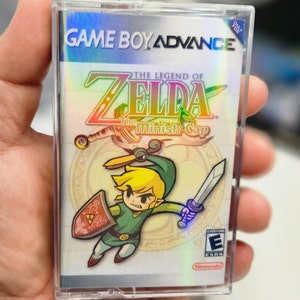 May include: A Game Boy Advance game cartridge for The Legend of Zelda: The Minish Cap. The cartridge is silver with a holographic image of Link, the main character, holding a sword and shield. The game is rated E for Everyone by the ESRB.