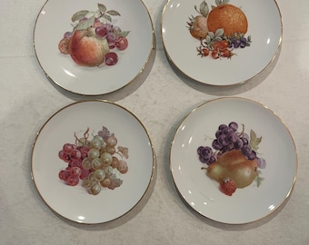 May include: Set of four white porcelain plates with gold rims, each featuring a different fruit illustration. The plates showcase a peach, orange, grapes, and a pear with a strawberry. A classic and elegant design for serving appetizers or desserts.