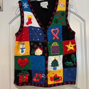 Può includere: Un gilet natalizio colorato con quadrati a tema vacanza. I quadrati presentano immagini di un pupazzo di neve, fiocchi di neve, un albero di Natale e regali. Il gilet ha uno sfondo nero con accenti rossi e bianchi.