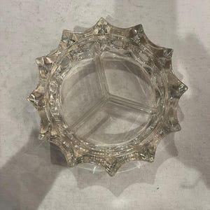 Puede incluir: Fuente de vidrio transparente con diseño de estrella. El plato está dividido en tres secciones y tiene un borde decorativo festoneado. El vidrio es transparente.
