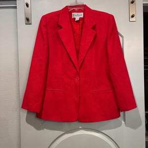 May include: A bright red blazer with a single-button closure, two front pockets, and a notched lapel. The blazer is hanging on a hanger. The label reads "Patchington Petite".