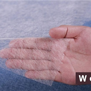 Puede incluir: Primer plano de una tela blanca, fina y tejida que se sostiene en una mano. La tela es muy delicada y tiene una apariencia suave, casi translúcida. La tela está etiquetada con "We fab" en la esquina inferior derecha.