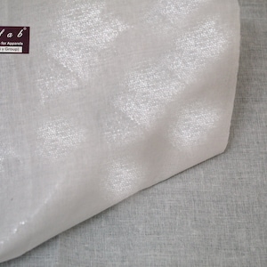 May include: Close-up of a white fabric with a subtle shimmer. The fabric is folded in half, revealing a slightly different texture on the underside. The fabric is labeled "Wefab Smartest Choice for Apparel (A Unit of a P Group)".