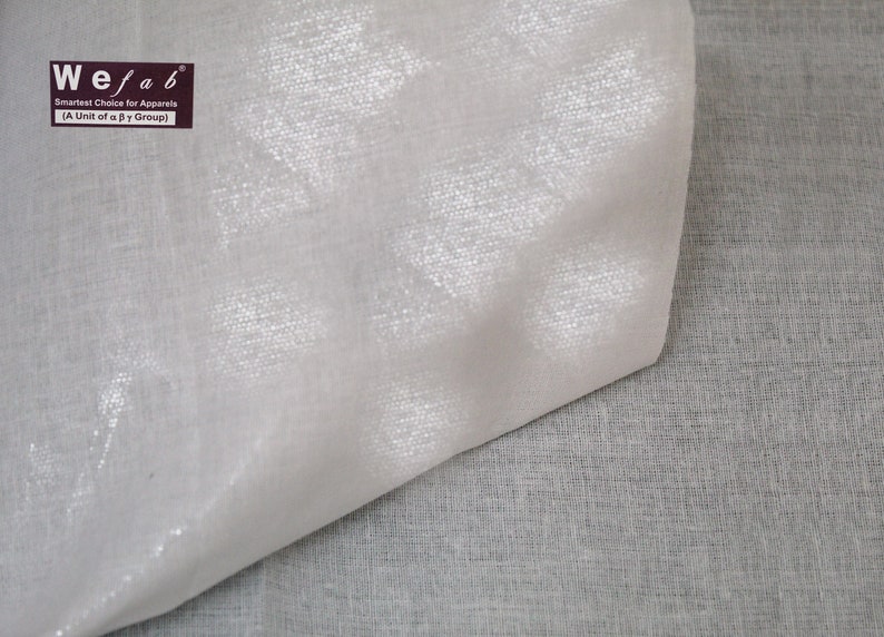 May include: Close-up of a white fabric with a subtle shimmer. The fabric is folded in half, revealing a slightly different texture on the underside. The fabric is labeled "Wefab Smartest Choice for Apparel (A Unit of a P Group)".