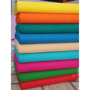 May include: A stack of fabric in various colors, including yellow, orange, green, blue, beige, turquoise, pink, and red. The fabric is folded neatly and stacked on top of each other.