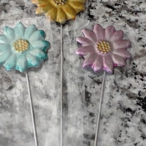 May include: Three decorative flower picks with metallic finishes. The flowers are yellow, blue, and pink. The picks are on a white background.