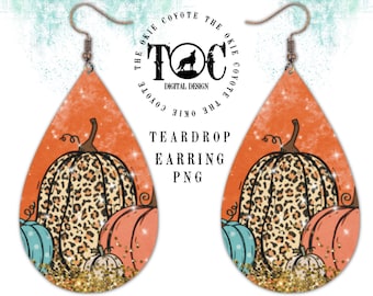 May include: A pair of teardrop-shaped earrings with a fall-themed design. The earrings feature a pumpkin with a leopard print pattern, surrounded by smaller pumpkins in shades of orange and blue. The background is a glittery orange.