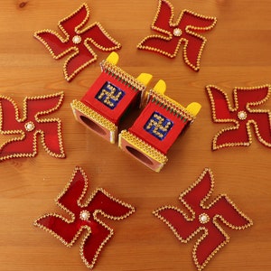 May include: Two small red and yellow painted wooden boxes with gold trim and a swastika symbol on each side. The boxes are surrounded by six red and gold swastika-shaped decorations.