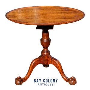 May include: A round, wooden table with a pedestal base and three cabriole legs ending in paw feet. The table is made of dark wood and has a smooth, polished finish.