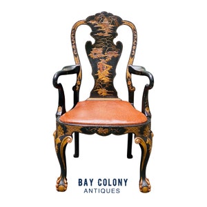 May include: A black and gold armchair with a carved wooden frame and a brown leather seat. The chair has a Chinese-inspired design with intricate details and a pagoda-like structure on the back.