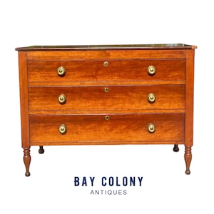 May include: A three-drawer chest of drawers made of wood with a rich mahogany finish. The chest has brass hardware and turned legs.  The chest is in good condition and has a classic design.