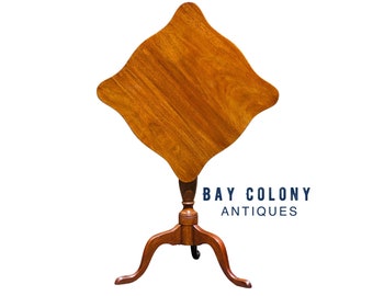 May include: A wooden, square-shaped, tilt-top table with a turned pedestal base and three cabriole legs. The table is made of a rich, reddish-brown wood.