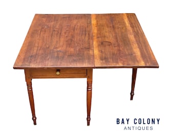 May include: A wooden drop-leaf table with a single drawer and turned legs. The table is made of a dark wood with a natural finish. The table is in good condition and has a rustic look.