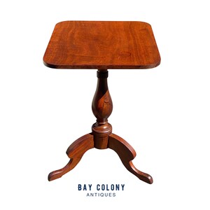 May include: A dark brown wooden side table with a square top and a pedestal base with three legs. The table is about 24 inches tall and 18 inches wide.  BAY COLONY ANTIQUES