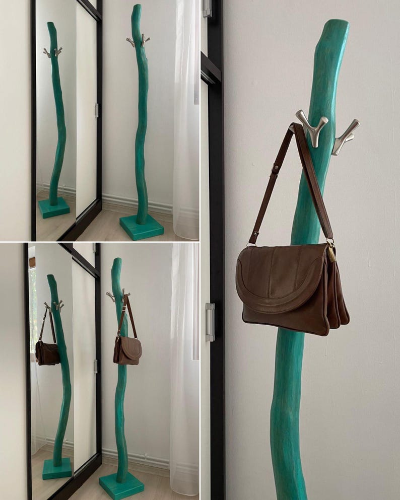 May include: A teal-colored, free-standing coat rack with a natural, curved design. The rack has multiple silver hooks and a square base. A brown leather shoulder bag hangs from one of the hooks.