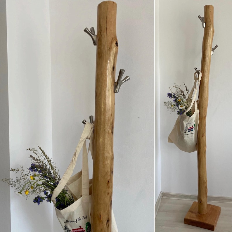 May include: A natural wood coat rack with multiple silver hooks. Two canvas tote bags hang from the hooks, filled with wildflowers. The rack is made from a tree trunk and stands on a square wooden base.