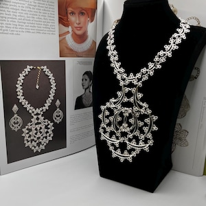 May include: A white ceramic mug with a black handle and the text "But First, Coffee" in a bold, black font. The mug is set against a blurred background, highlighting its clean design.