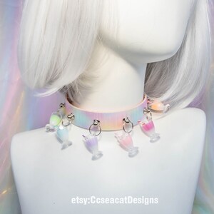 May include: A pastel pink choker with a rainbow tie-dye pattern and multiple clear plastic charms shaped like glasses with colourful liquids inside. The choker is on a white mannequin with white hair. The text "etsy:CcseacatDesigns" is at the bottom of the image.