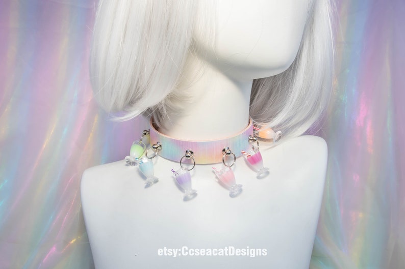 May include: A pastel pink choker with a rainbow tie-dye pattern and multiple clear plastic charms shaped like glasses with colourful liquids inside. The choker is on a white mannequin with white hair. The text "etsy:CcseacatDesigns" is at the bottom of the image.