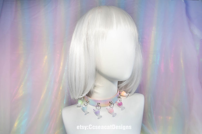 May include: A pastel rainbow choker with a white base and silver rings. The choker has multiple charms hanging from it, each charm is a different colour and shaped like a glass of juice. The text "etsy:CcseacatDesigns" is visible at the bottom of the image.