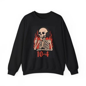 Op de afbeelding: Zwart sweatshirt met een grafische print van een skelet met een koptelefoon op en een duim omhoog. Het skelet is omringd door vlammen en de tekst "10-4" is eronder gedrukt.