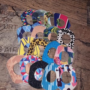 Può includere: Una collezione di cerotti adesivi a motivi vari, tra cui forme geometriche, stampe animalier e motivi astratti. Le toppe sono disposte su una superficie di legno, mostrando una varietà di colori e trame.