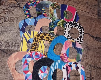Può includere: Una collezione di cerotti adesivi a motivi vari, tra cui forme geometriche, stampe animalier e motivi astratti. Le toppe sono disposte su una superficie di legno, mostrando una varietà di colori e trame.